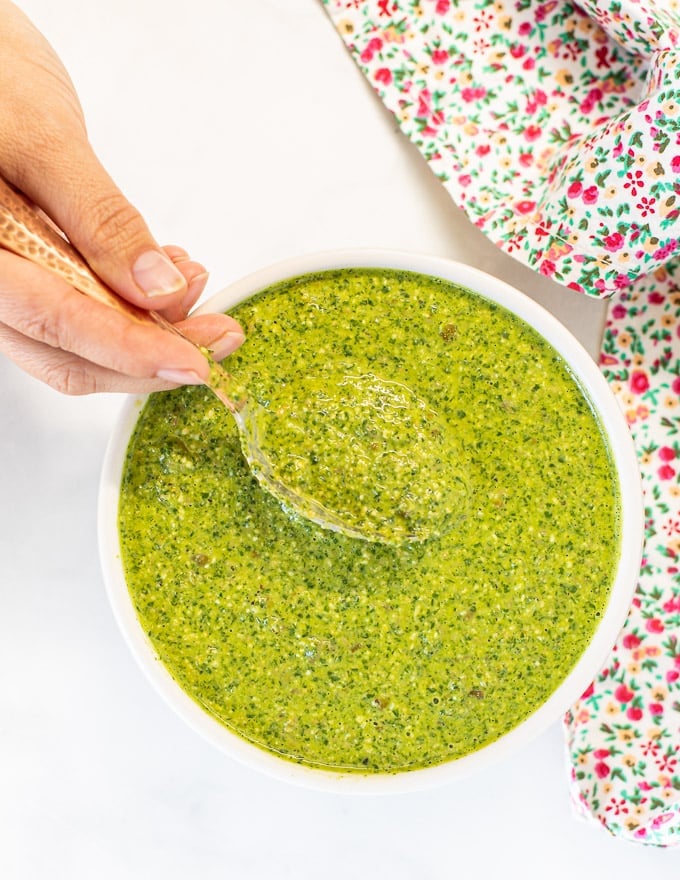 herby green sauce in a bowl with someone scooping out a spoonful. Photo taken from above. 