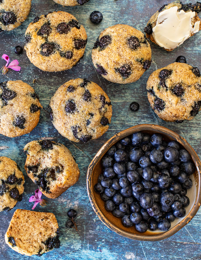 over head shot of a bowl of fresh blueberries and vegan blueberry muffins, a couple split and one buttered