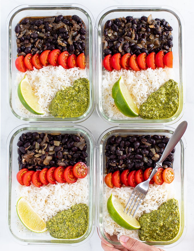 4 glass vegan meal prep containers with rice, black beans, tomatoes and green sauce 