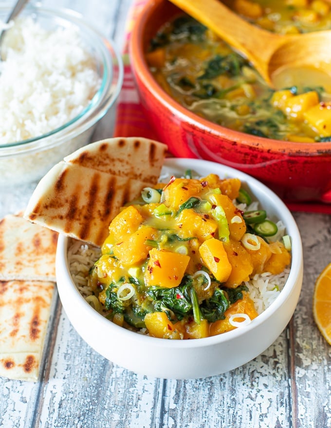 a small bowl of butternut squash curry over rice with a wedge of naan bread on the side