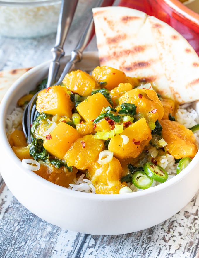 close up shot of butternut squash curry in a white bowl with a wedge of naan bread 