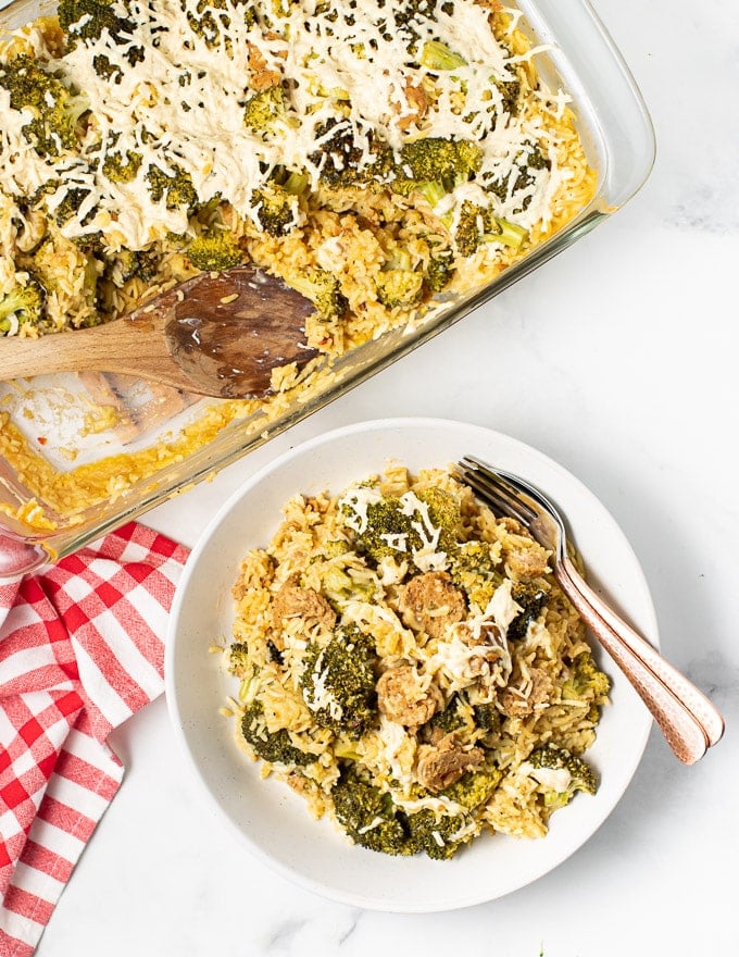 a dish of vegan broccoli rice casserole next to a bowl full with a fork and spoon on the side 