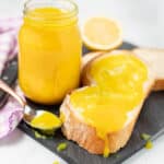 een pot van vegan lemon curd op een leistenen bord met een sneetje brood