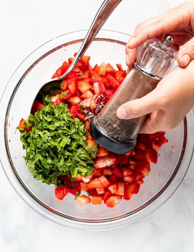 black pepper being ground into strawberry salsa