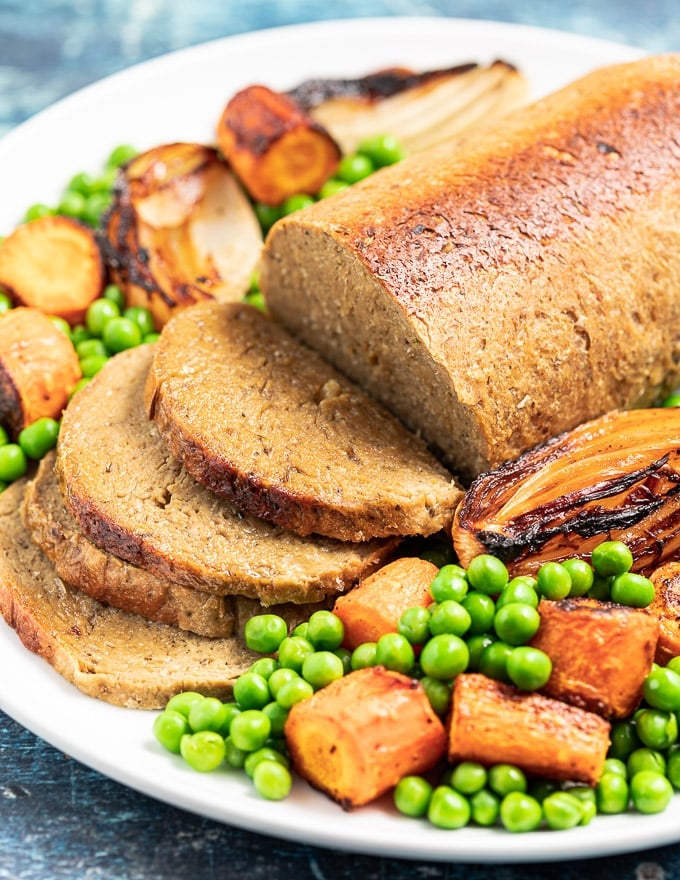 A vegan roast, part sliced, on a platter with vegetables