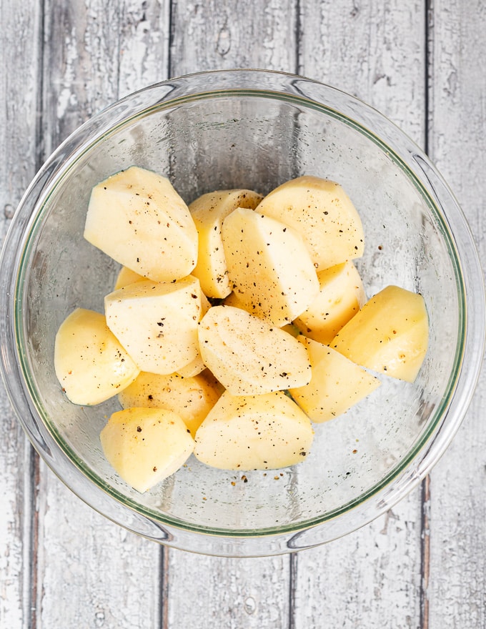a bowl of raw potato pieces tossed in oil and salt and pepper