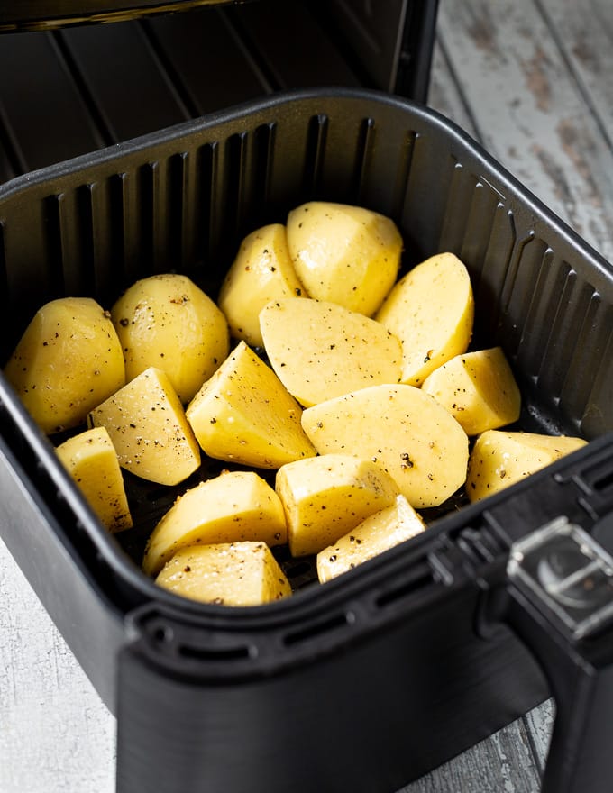 seasoned raw potatoes in the basket of an air fryer