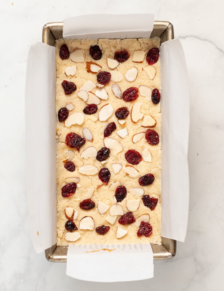 flaked almonds and dried cranberries pressed into uncooked vegan shortbread in a loaf pan