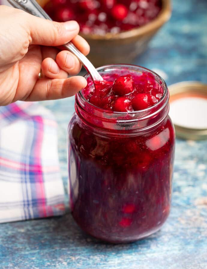 an open jar of Instant pot Cranberry Sauce with someone scooping out a spoon full