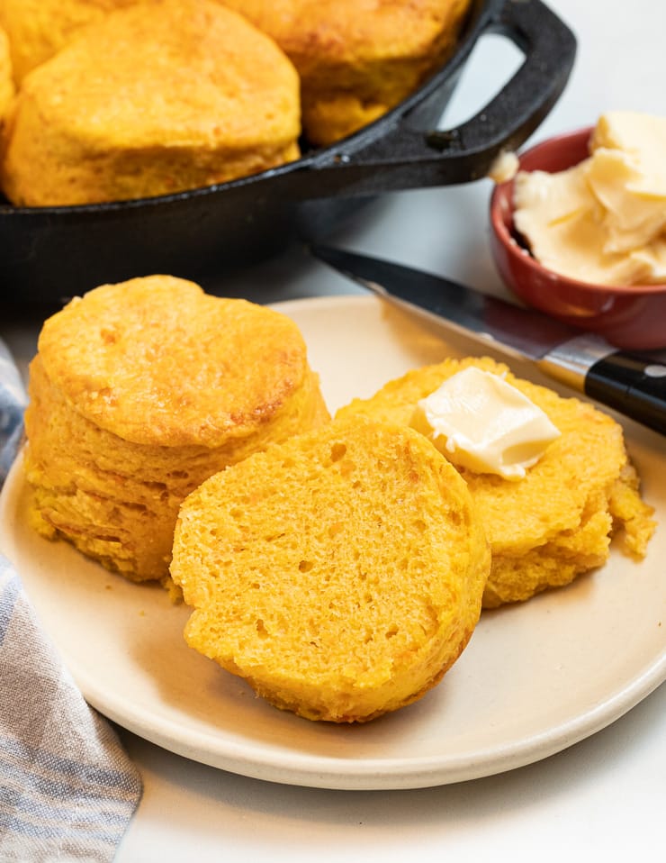 vegan sweet potato biscuits on a plate. One cut with vegan butter on one side