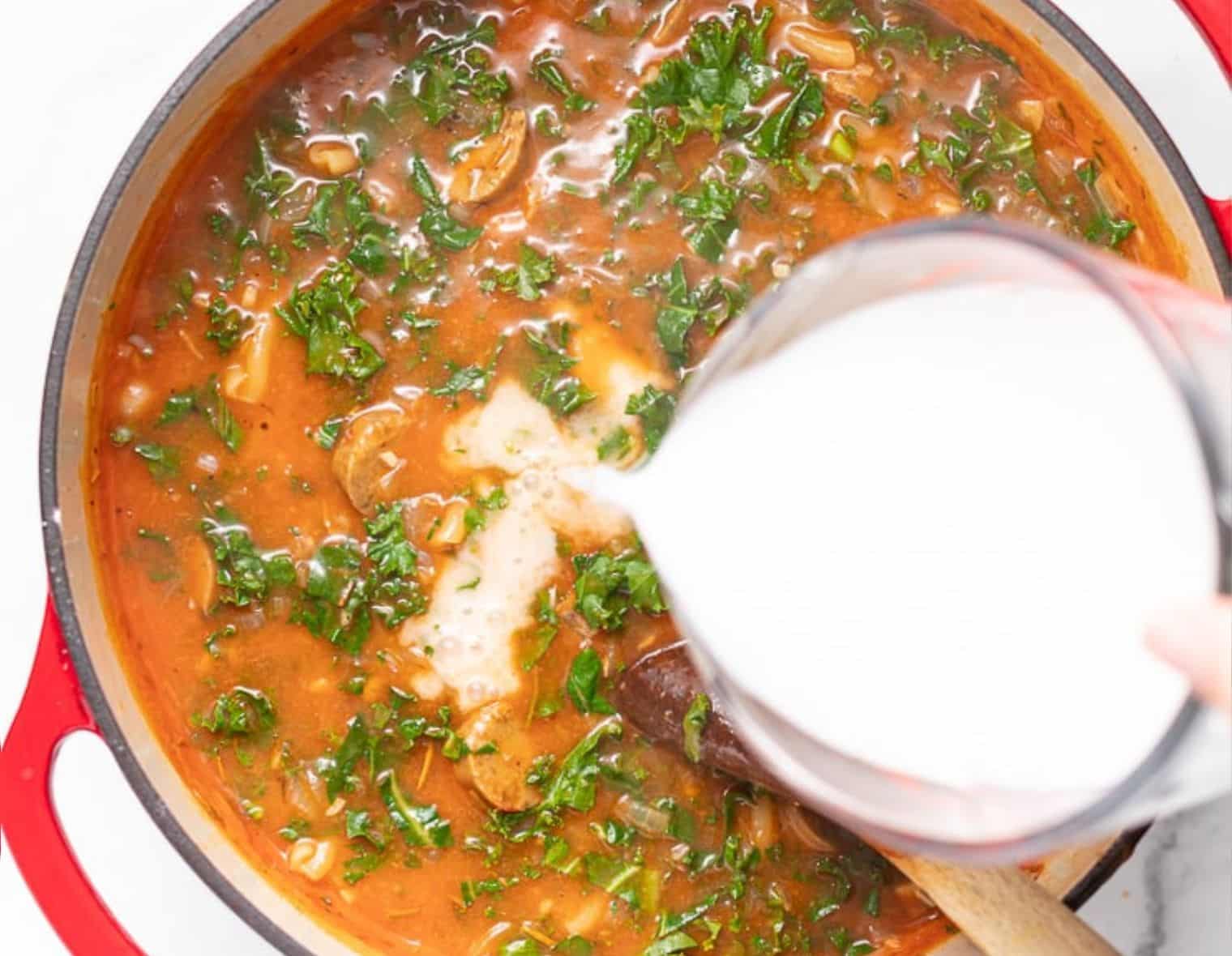 coconut milk being poured into a pan of soup