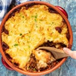 Lentil Shepherd's Pie w naczyniu z terakoty z drewnianą łyżką zagłębiającą się w środku's Pie in a terracotta dish with a wooden spoon digging in