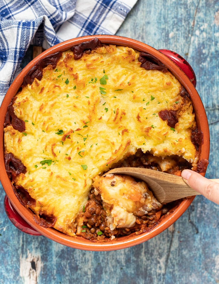 Lentil Shepherd's Pie w terakotowym naczyniu z drewnianą łyżką, w której można się zagłębić's Pie in a terracotta dish with a wooden spoon digging in