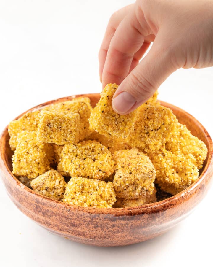 crispy tofu pieces in a brown bowl with a hand taking one