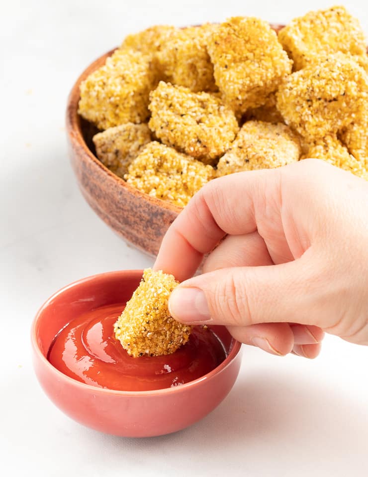 a piece of crispy tofu being dipped in tomato ketchup