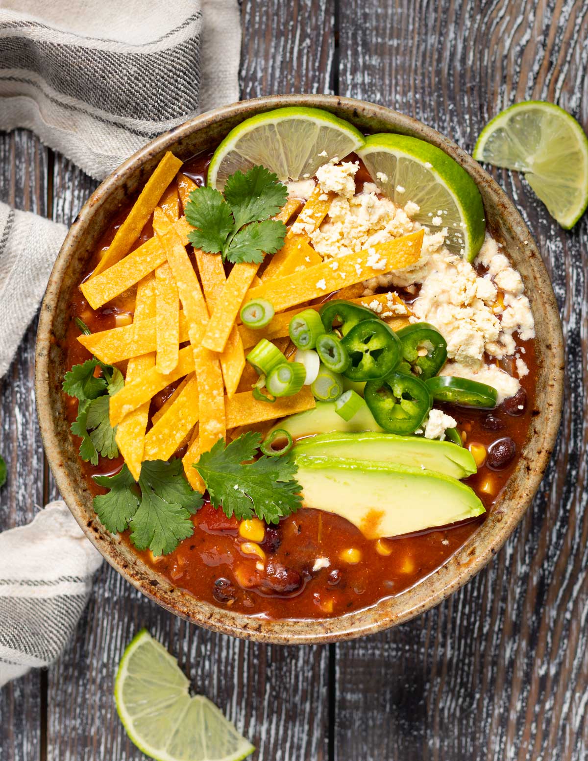 a bowl of topping heavy vegan tortilla soup on a wooden backdrop with some lime slices