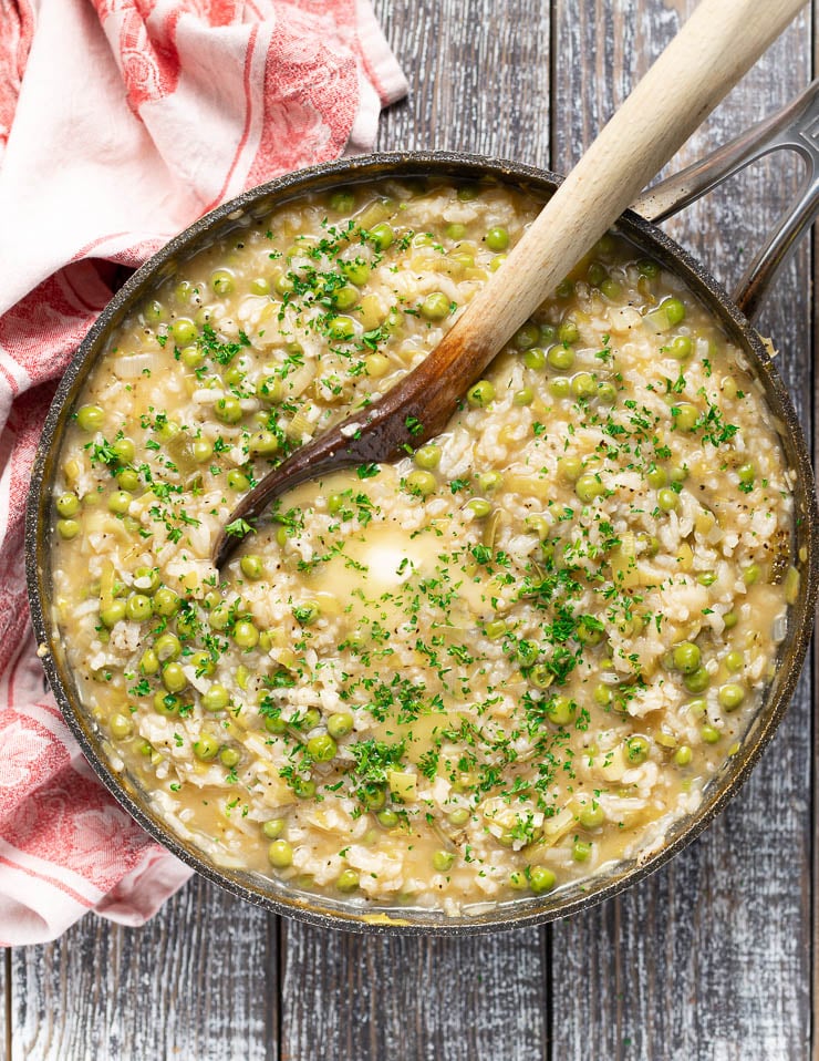 Creamy Risi e Bisi (Italian rice and peas) in a pan and topped with melty vegan butter and fresh parsley