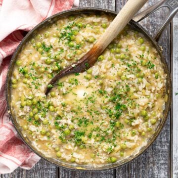 cooked risi e bisi (Italian rice and peas) in a pan topped with some melting butter and fresh chopped parsley