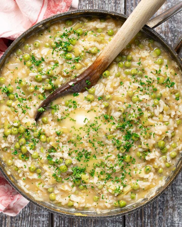 cooked risi e bisi (Italian rice and peas) in a pan topped with some melting butter and fresh chopped parsley