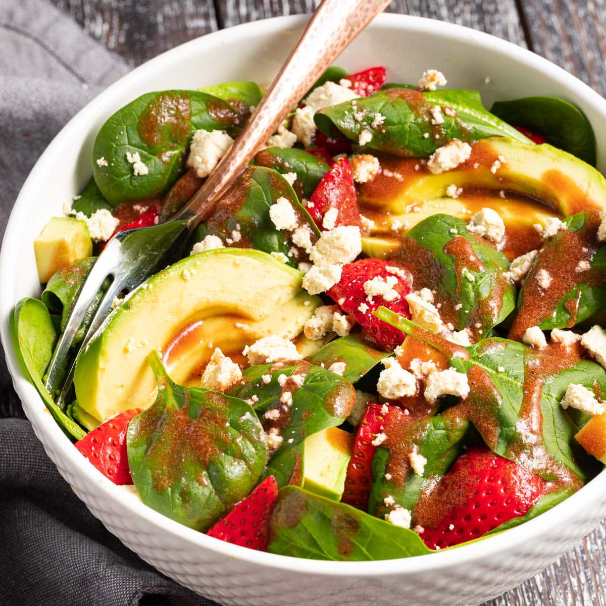 a bowl of strawberry spinach salad with avocado and vegan feta drizzled in strawberry vinaigrette