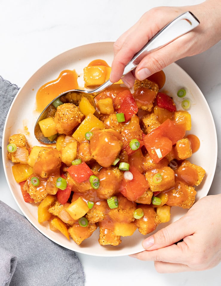 someone holding a plate of sweet and sour tofu