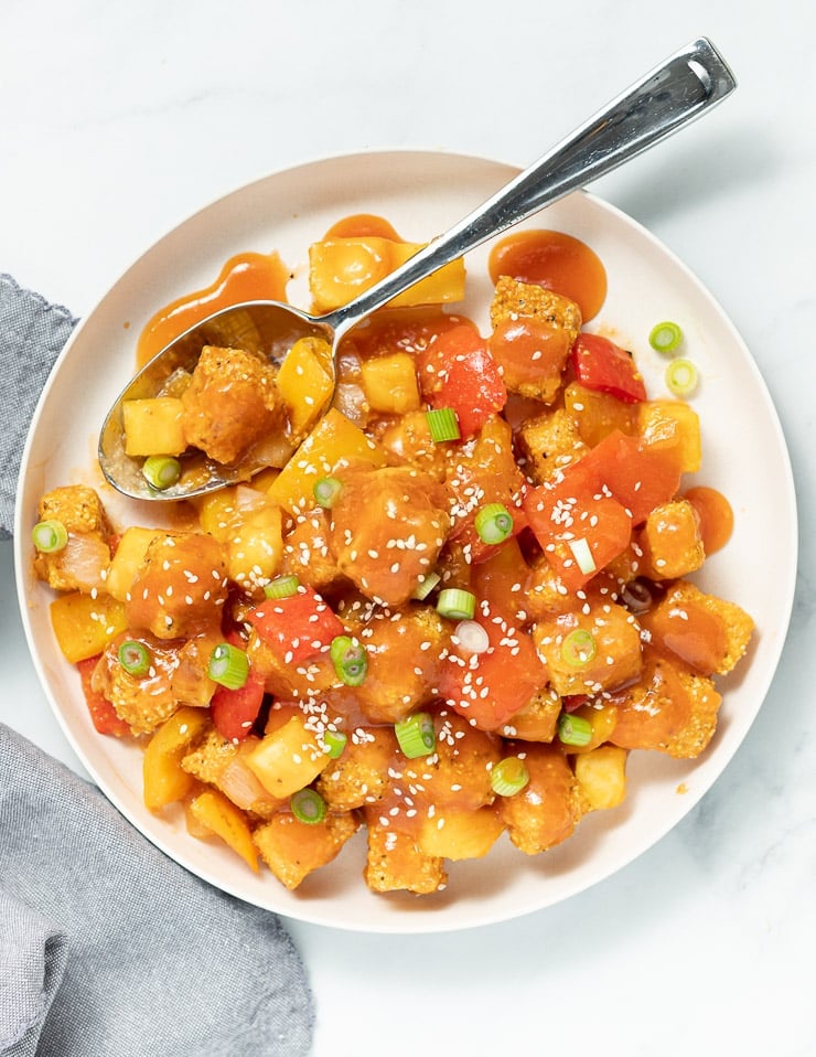 sweet and sour tofu with sesame seeds on a large white place with a spoon