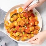 hands holding a plate of sweet and sour tofu