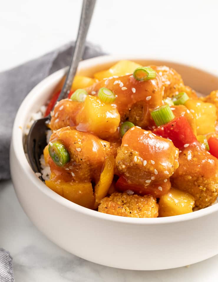 a bowl of crispy tofu and healthy sweet and sour sauce in a bowl with a sprinkle of sesame seeds and green onions