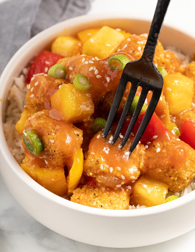 a fork digging in to a bowl of sweet and sour tofu 