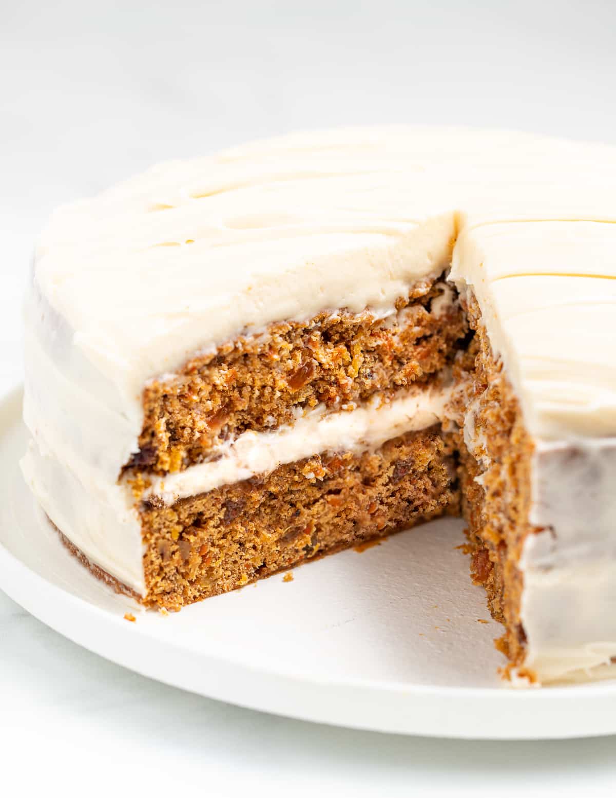 a vegan carrot cake on a plate with one slice cut out, inside showing