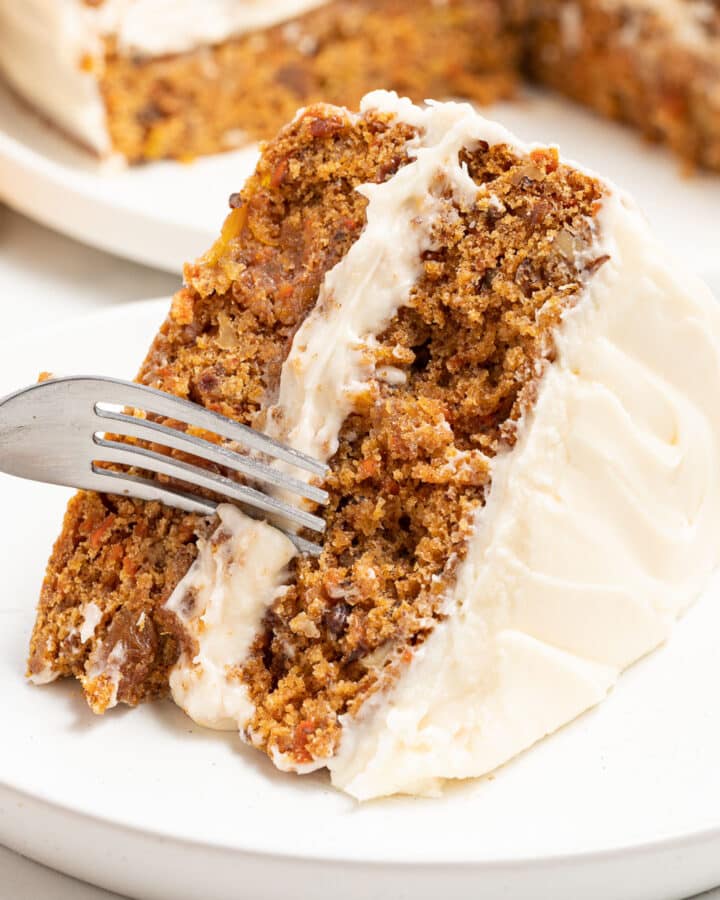 a slice of frosted vegan carrot cake on a plate