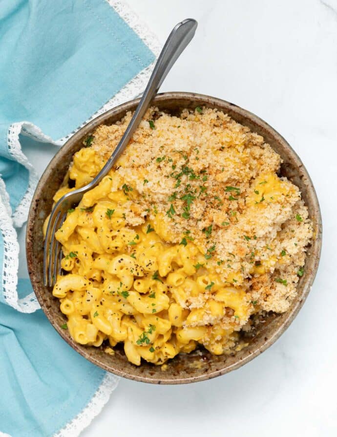 a bowl of vegan mac and cheese in a bowl with a fork on the side and a sprinkle of parsley
