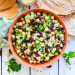 a bowl of kidney bean salad with some salad servers and pita breads