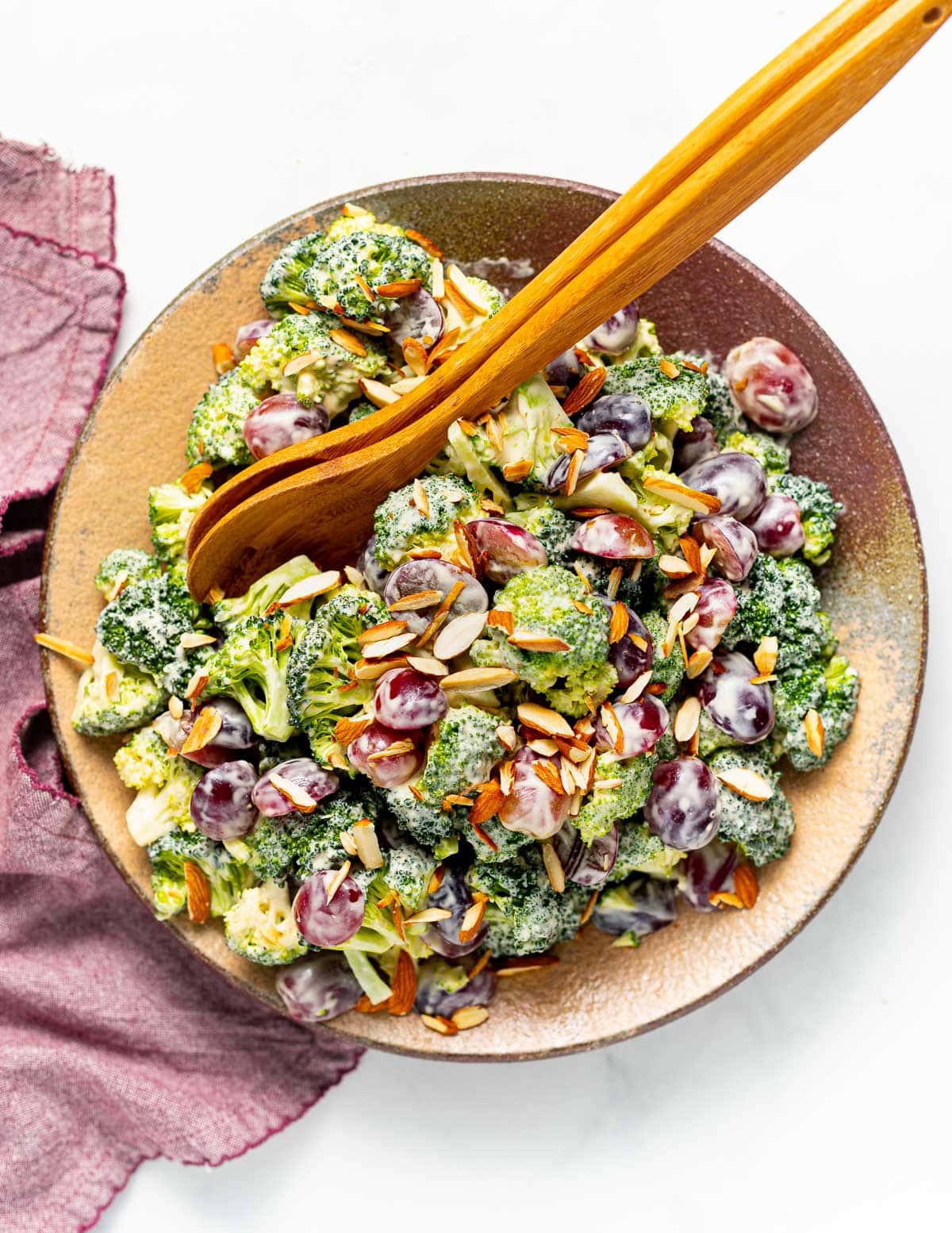 a plate of vegan broccoli salad with wooden salad servers resting across it