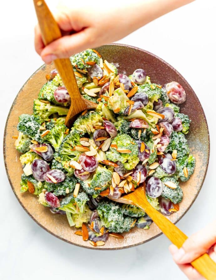 2 salad servers digging in to a vegan broccoli salad - taken from above