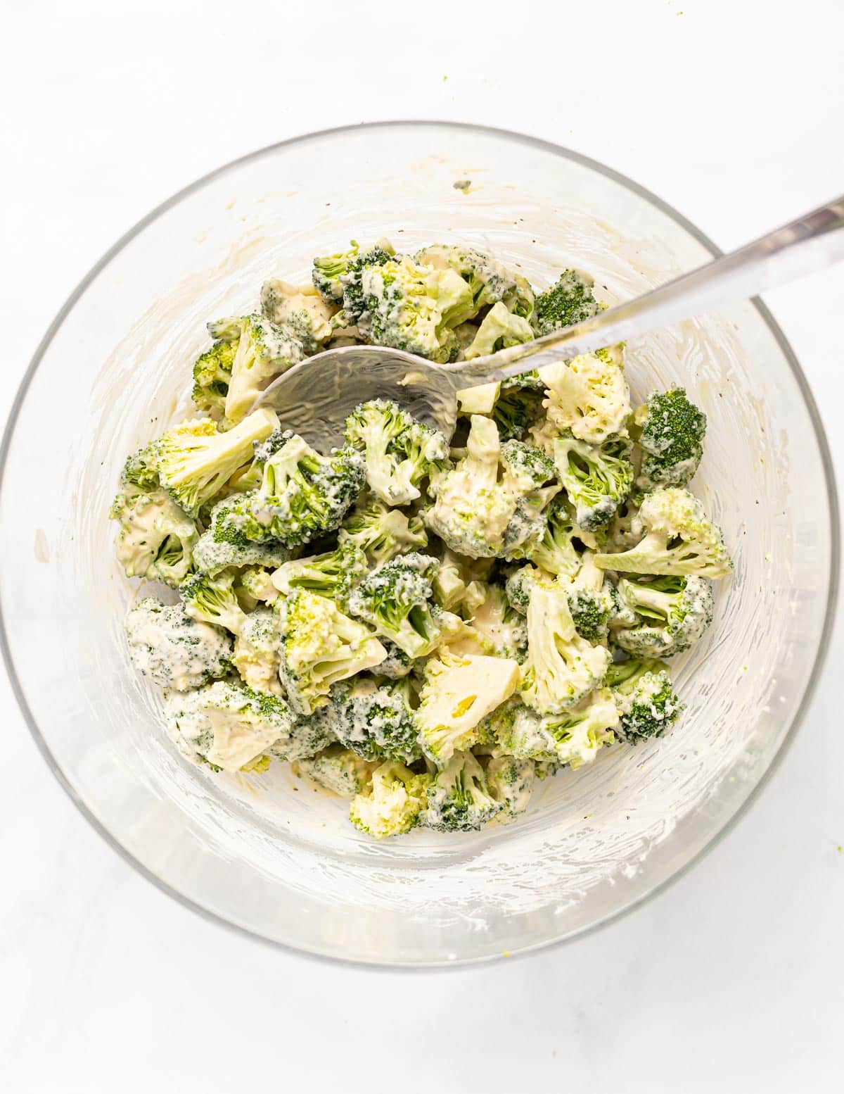 a bowl of raw broccoli florets tossed in a creamy dressing 