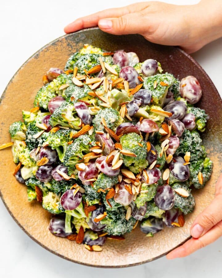 hands holding a plate of vegan broccoli salad