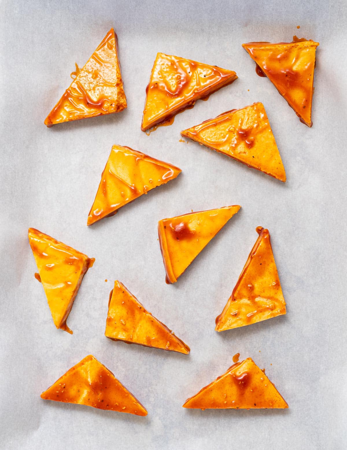 uncooked glazed triangles of tofu on a lined baking tray 