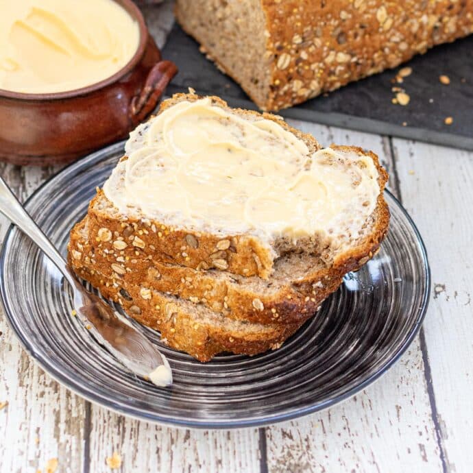 3 slices of bread stacked on a plate. Top slice thickly buttered with a small bite taken out