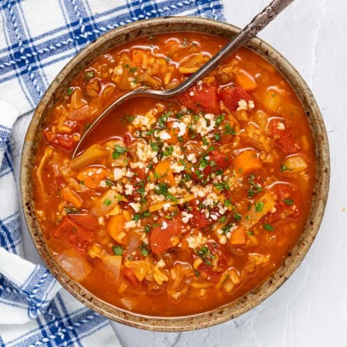 a bowl of vegan cabbage soup with chopped herbs and crumbled cheese on top