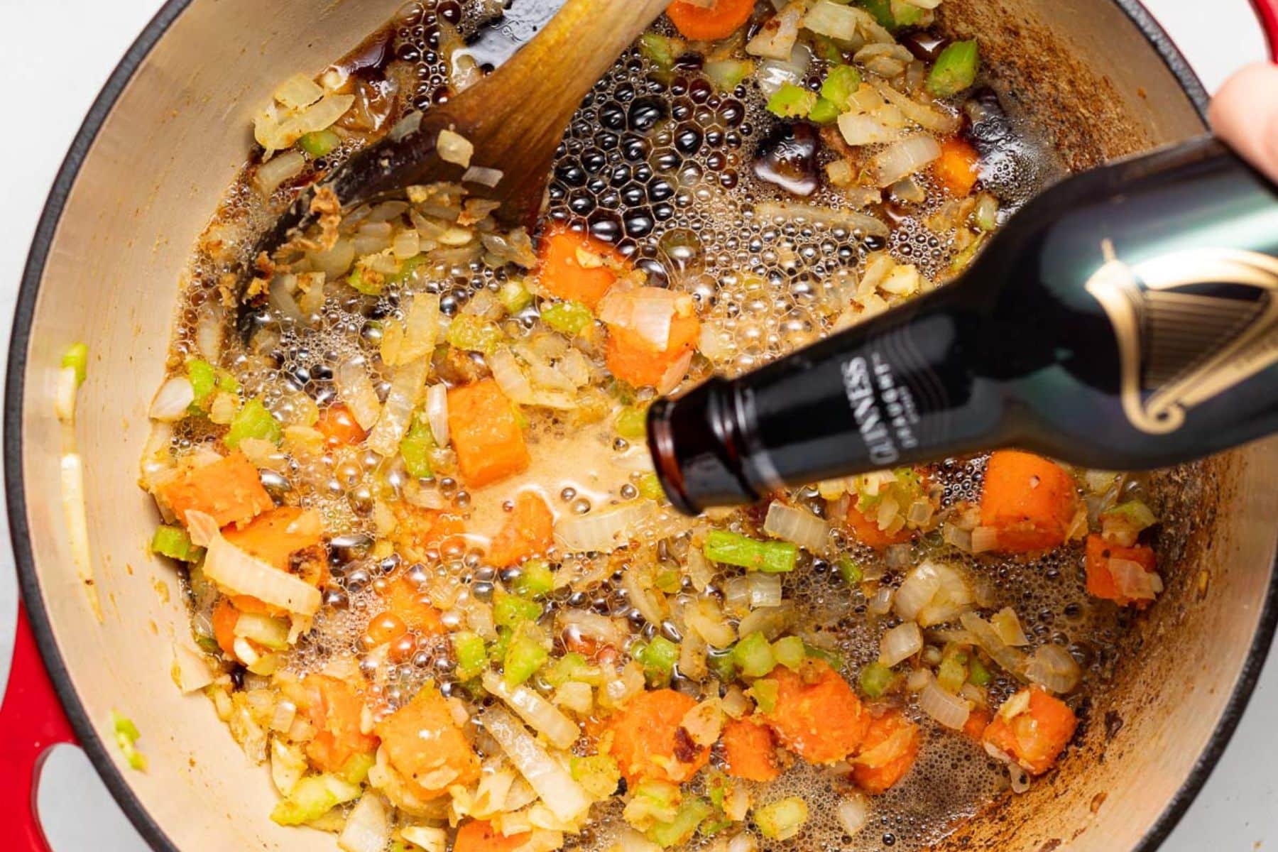 Guinness pouring into a Dutch oven with sauteeed vegetables. 