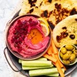 beet hummus in a bowl surrounded by flatbread and veg