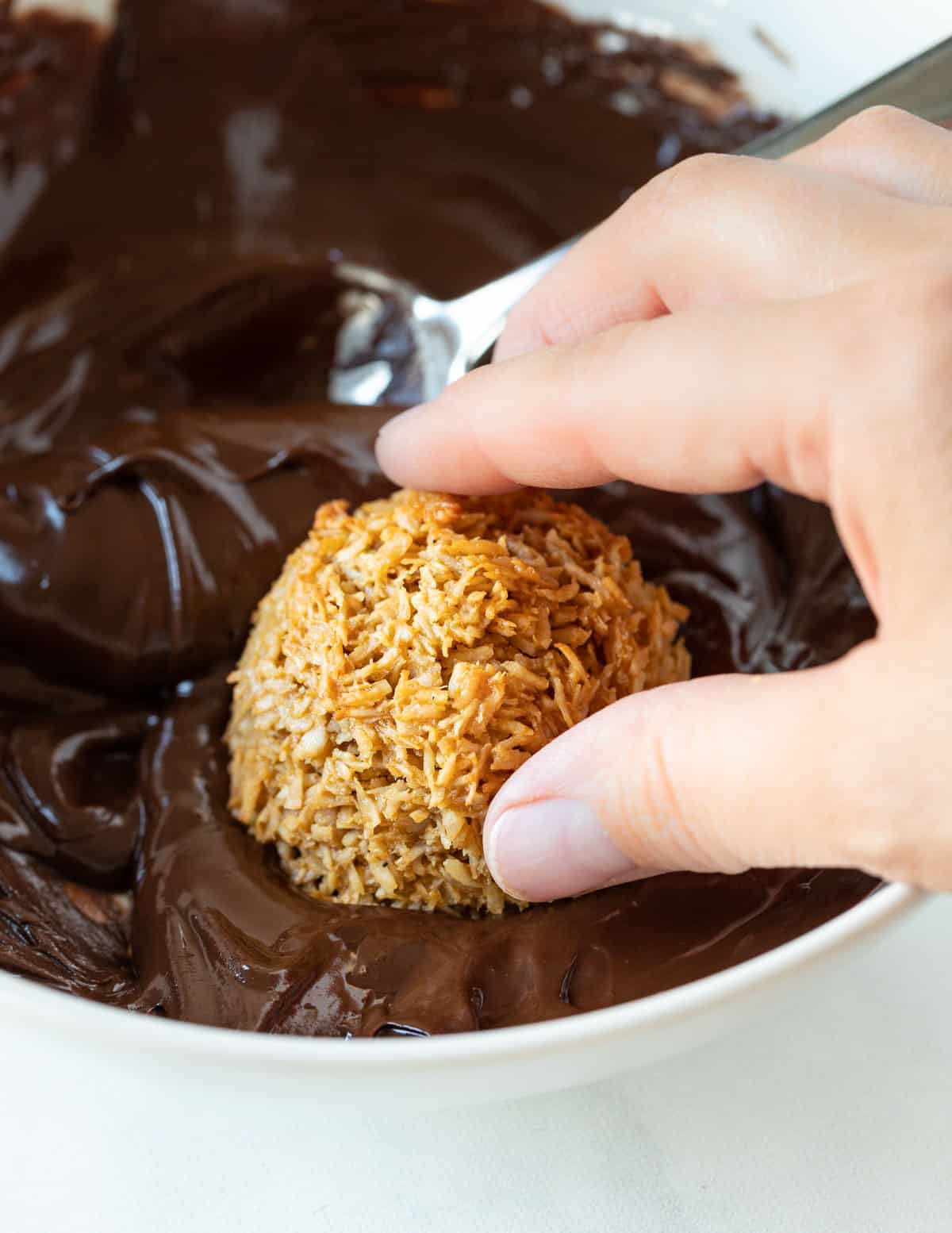 a coconut macaroon being dipped into a bowl of chocolate