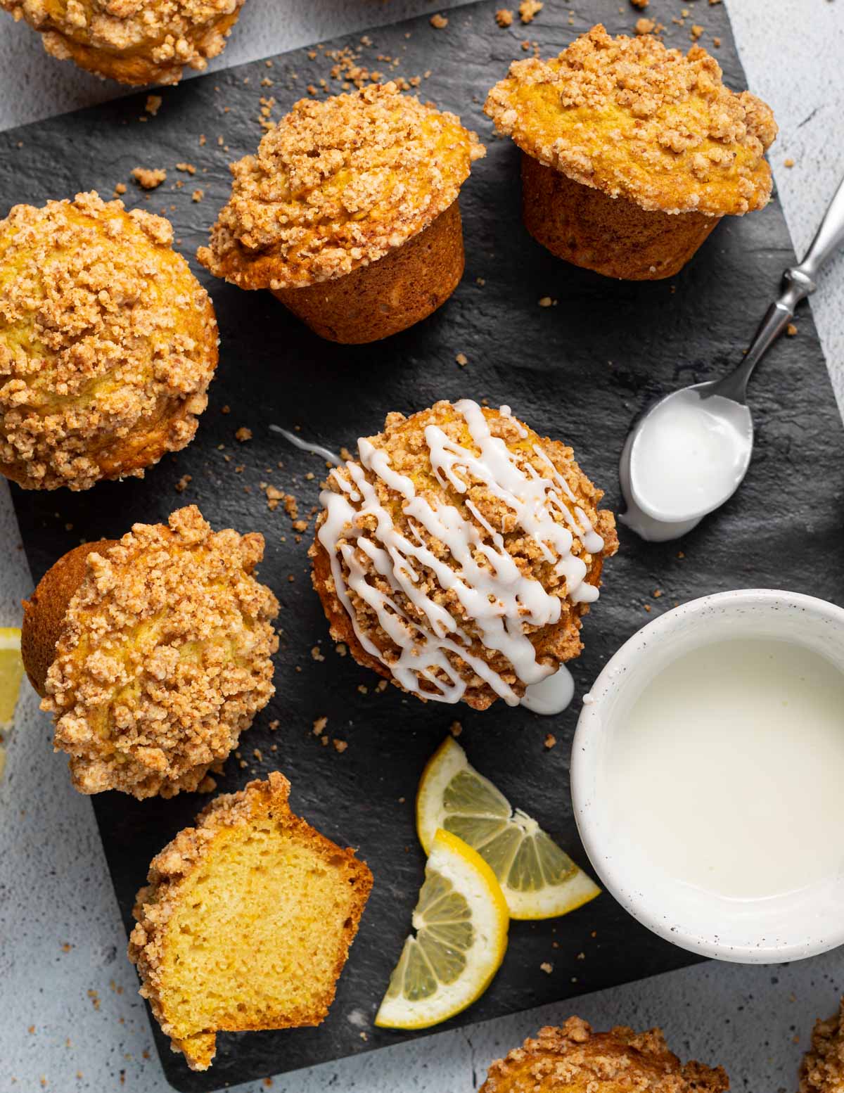 vegan lemon muffins on a slate board with a bowl of glaze