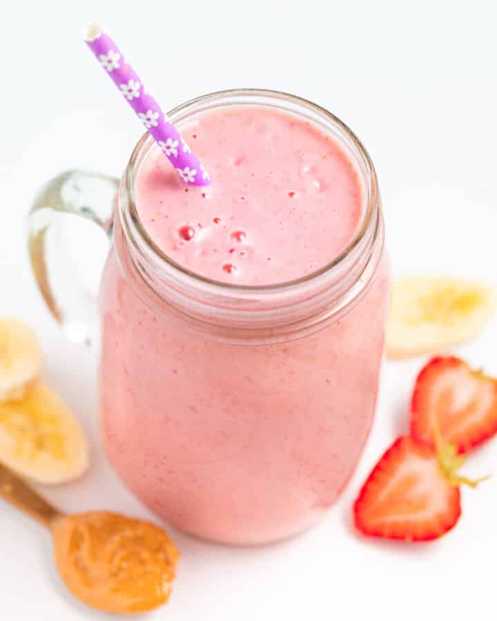 a strawberry banana peanut butter smoothie in a glass with a straw