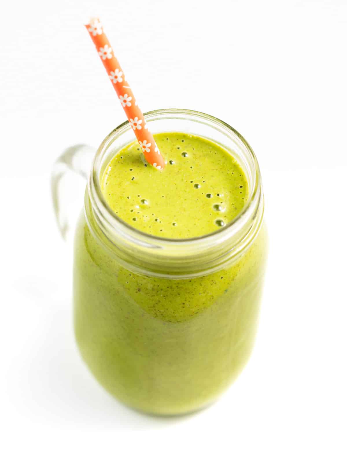 a glass of vegan green smoothie with an orange straw