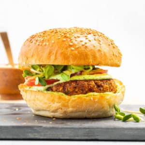 a kidney bean burger patty in a bun with green sauce, sprouts and tomato