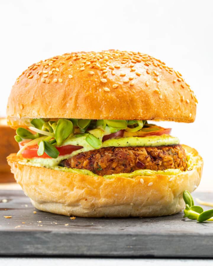 a kidney bean burger patty in a bun with green sauce, sprouts and tomato