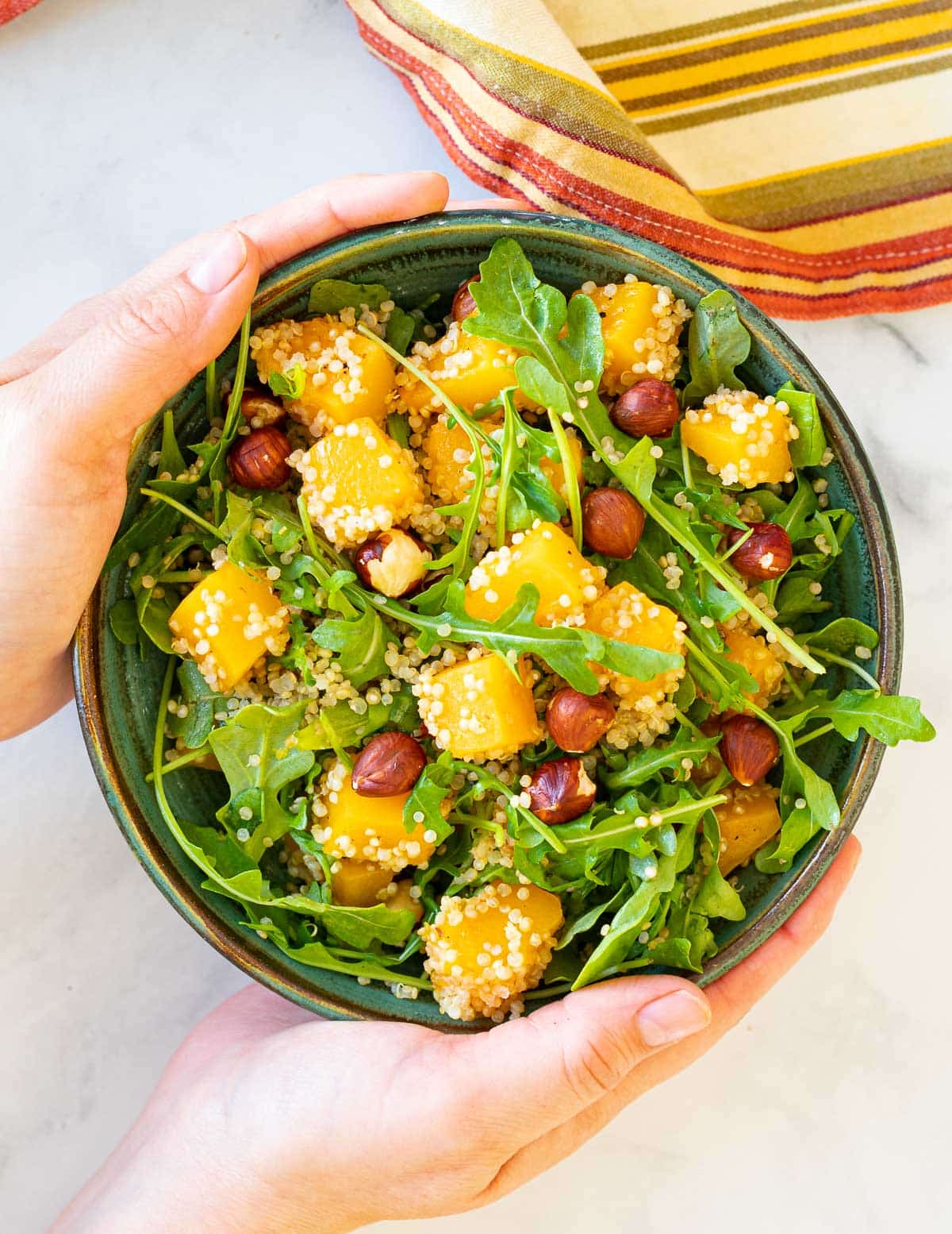 a bowl of quinoa butternut squash salad held by 2 hands