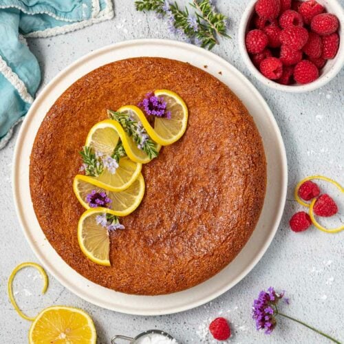 vegan almond cake on a plate topped with swirly lemon slices and purple flowers